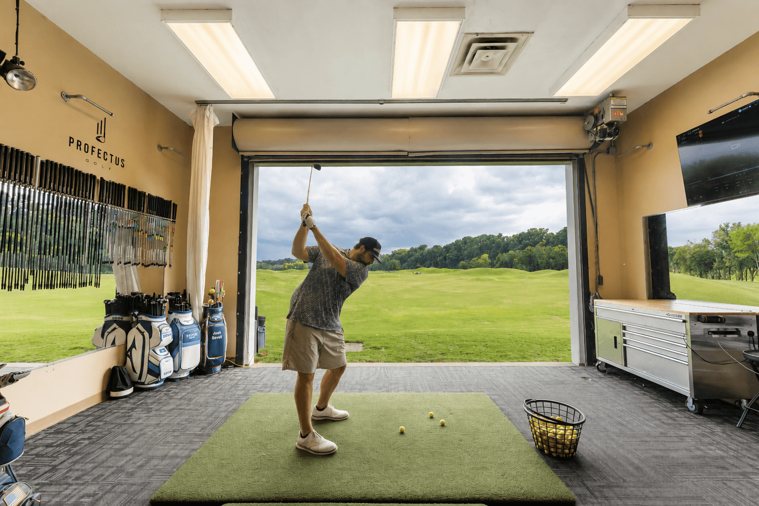 A golfer practicing in the bright indoor-outdoor hitting bay at Profectus Golf